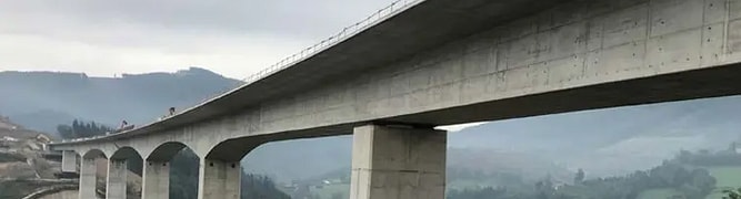 A long concrete viaduct under construction curving through a green, hilly landscape