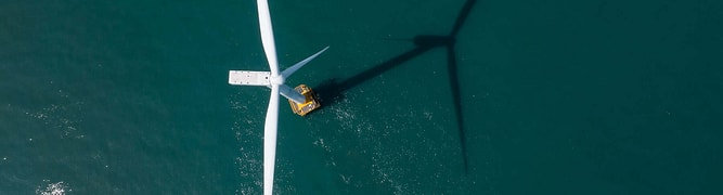 Aerial view of an offshore wind turbine with a maintenance vessel nearby, casting a long shadow across the water—ideal for integrating substation data to optimize operations and ensure efficient energy transmission.