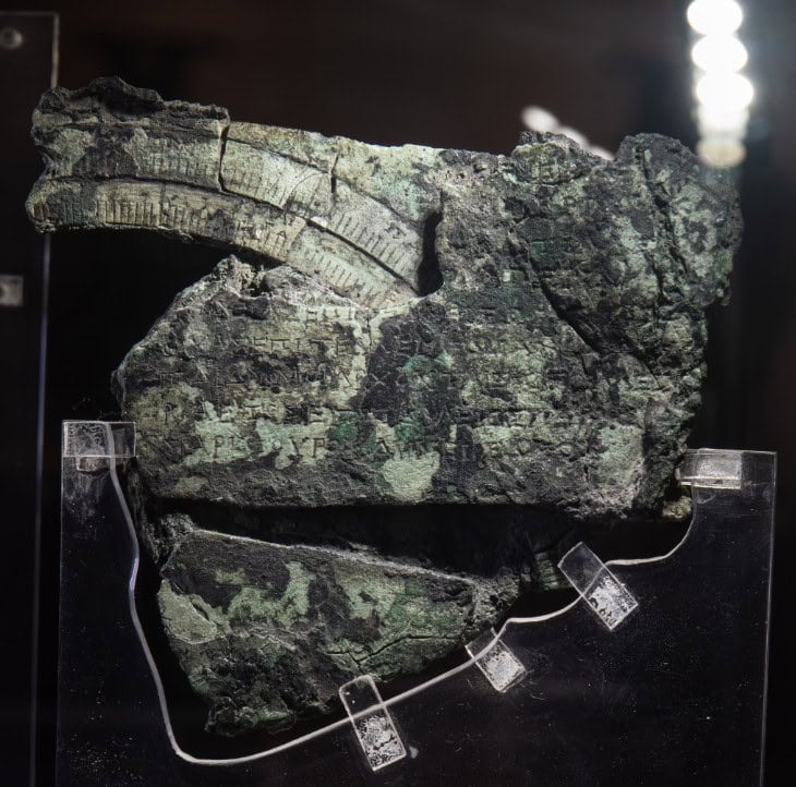 Fragment of the Antikythera mechanism, often regarded as an ancient computer, displayed on a stand with visible gears and inscriptions.
