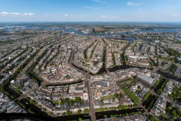 Aerial view of a city with concentric canals and streets, lined with buildings and green trees, under a clear sky.