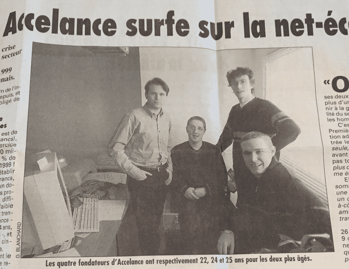 Four young men pose together in an office setting, surrounded by boxes and computers, as featured in a French newspaper article.
