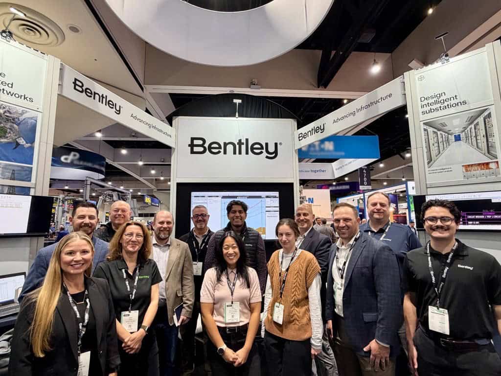 A group of people stands and smiles in front of a Bentley booth at a convention or trade show, with display screens and signage visible in the background.