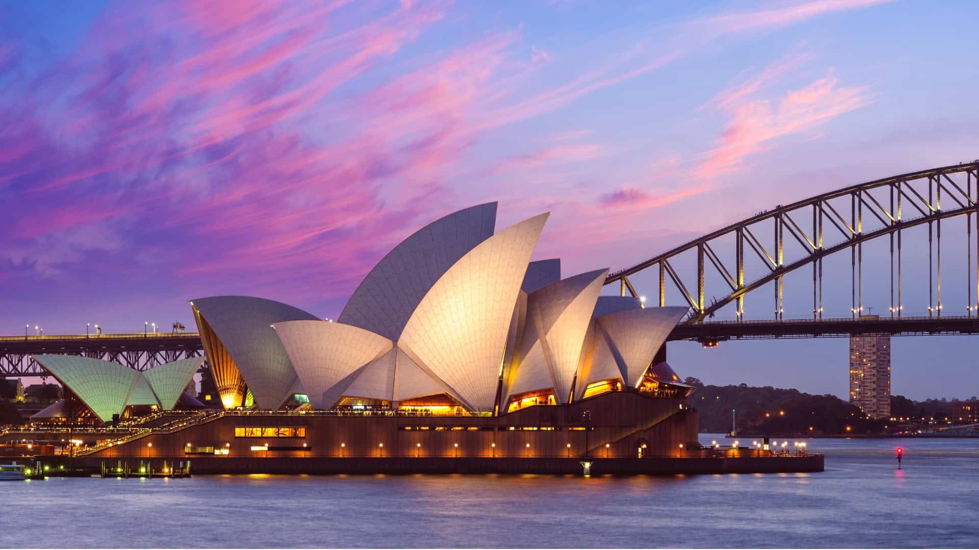 Sydney Opera House and Harbour Bridge at dusk with a colorful sky, viewed from across the water&mdash;an iconic example of how infrastructure can inspire reinvention and connect a city through architecture.