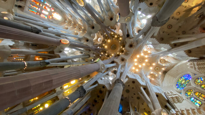 View looking up at the ornate ceiling and columns inside the Sagrada Fam&iacute;lia basilica, showcasing how visionary design and build techniques create stunning stained glass windows and intricate architectural details.