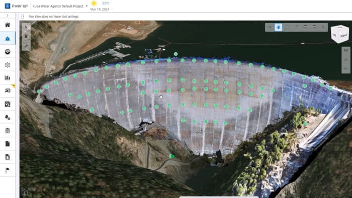 Aerial view of a large dam with monitoring points marked by green dots; water on one side, infrastructure visible on the other.