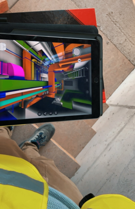 A person holds a tablet, displaying piping on a graphical interface