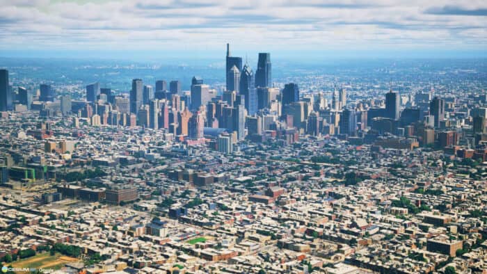 Aerial view of a city with a dense cluster of high-rise buildings in the center, surrounded by lower residential and commercial structures, under a partly cloudy sky.