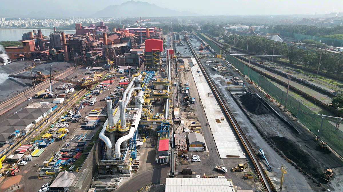 Aerial view of an industrial complex with large machinery, factories, and construction work alongside rail tracks and storage areas.