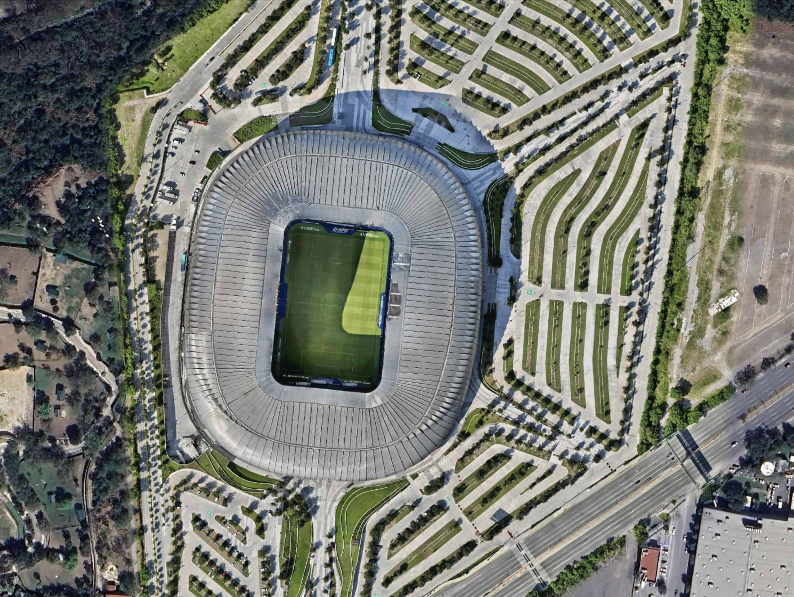 Aerial view of a large, oval-shaped World Cup Stadium with a green field in the center, surrounded by empty parking lots and roads.