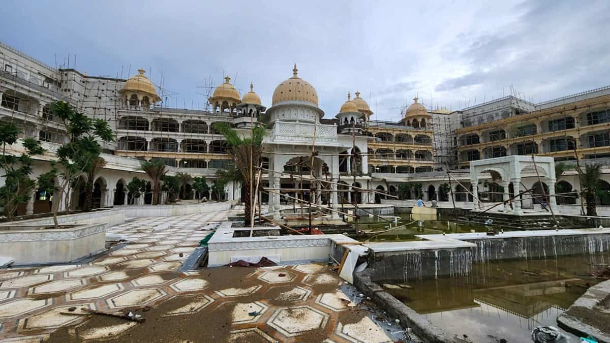 A large, ornate building with domes under construction by ISID STRUCTURES, surrounded by scaffolding, with an empty and unfinished fountain area in the foreground.