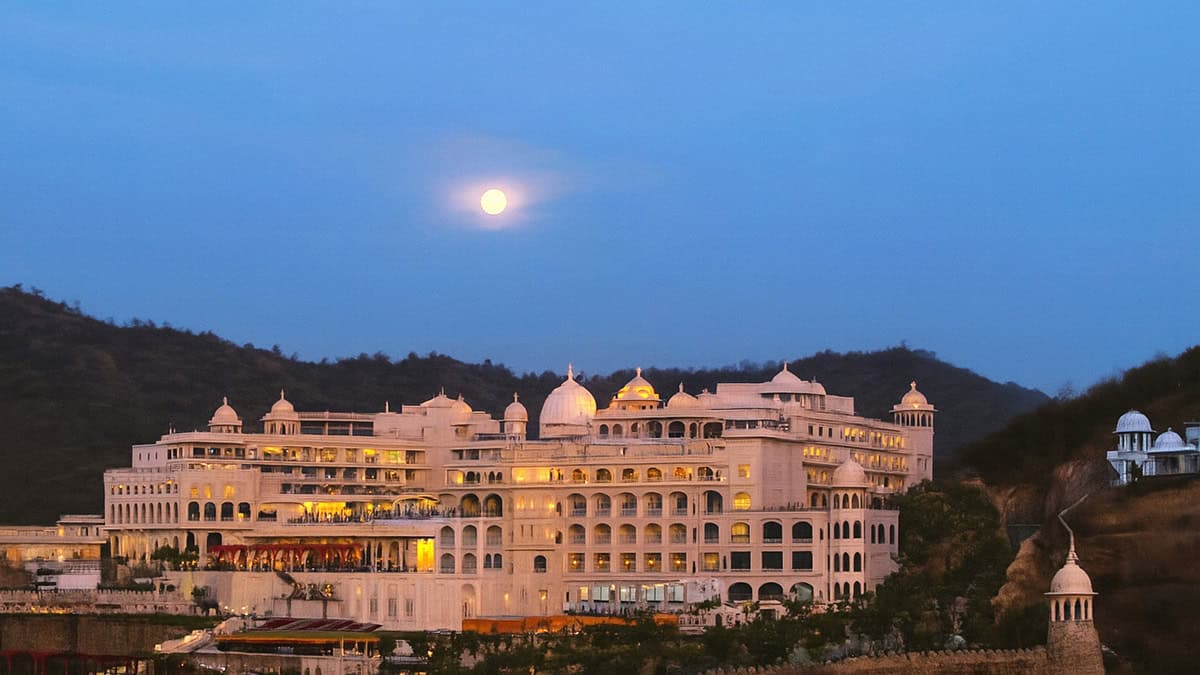 Large illuminated white building with domes and arches set against hills at dusk, with a full moon visible in the evening sky—this is the stunning Fairmont Palace Udaipur, a YII Winner designed with AVS ENGINEERS’ expertise.