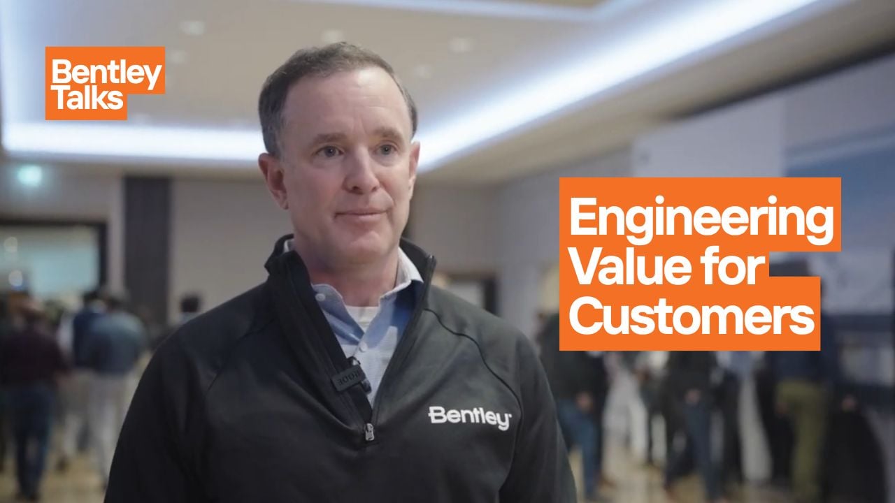 A man in a Bentley-branded jacket speaks at an event focused on business value.