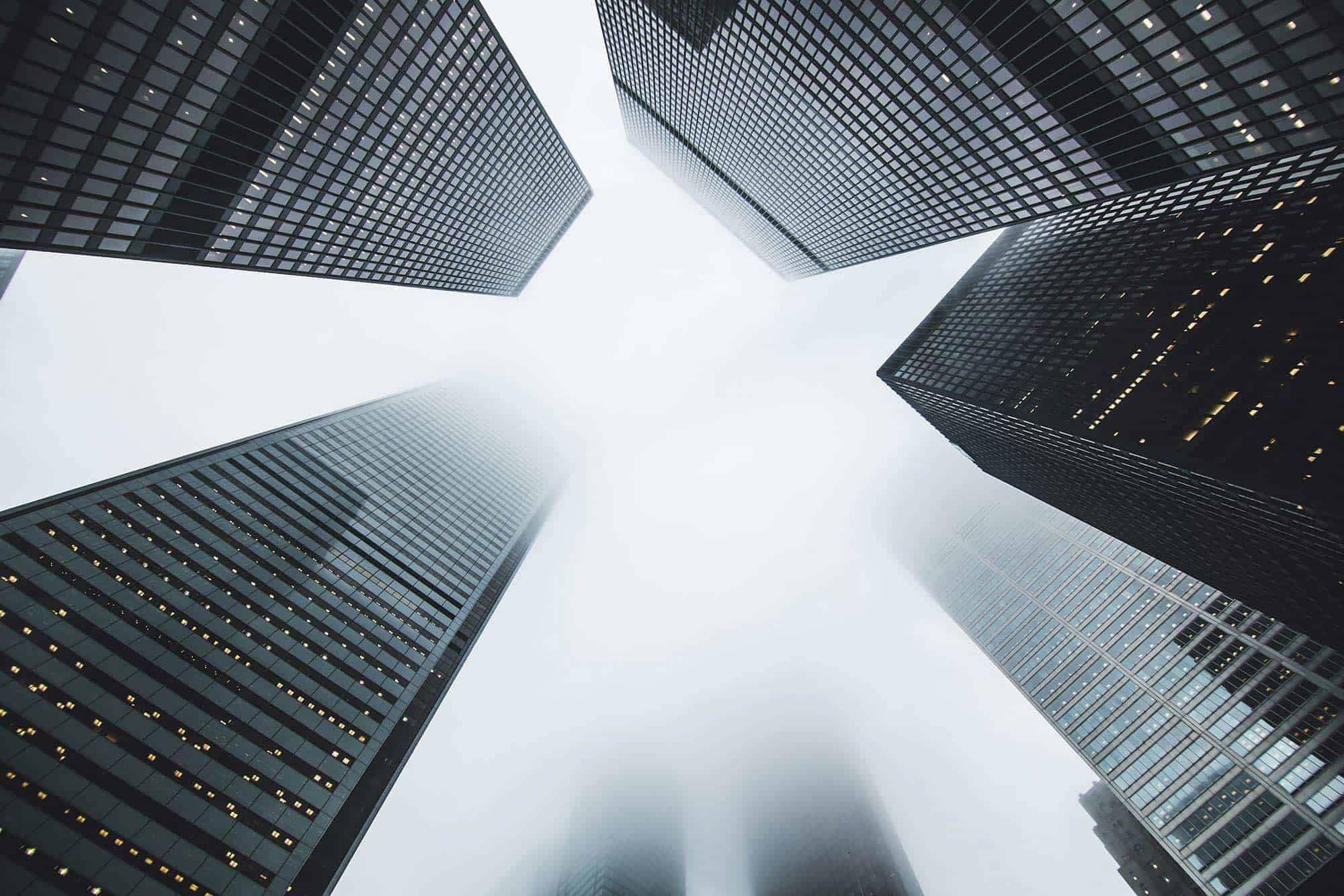 pedestrian view of tall buildings stretching up in the clouds