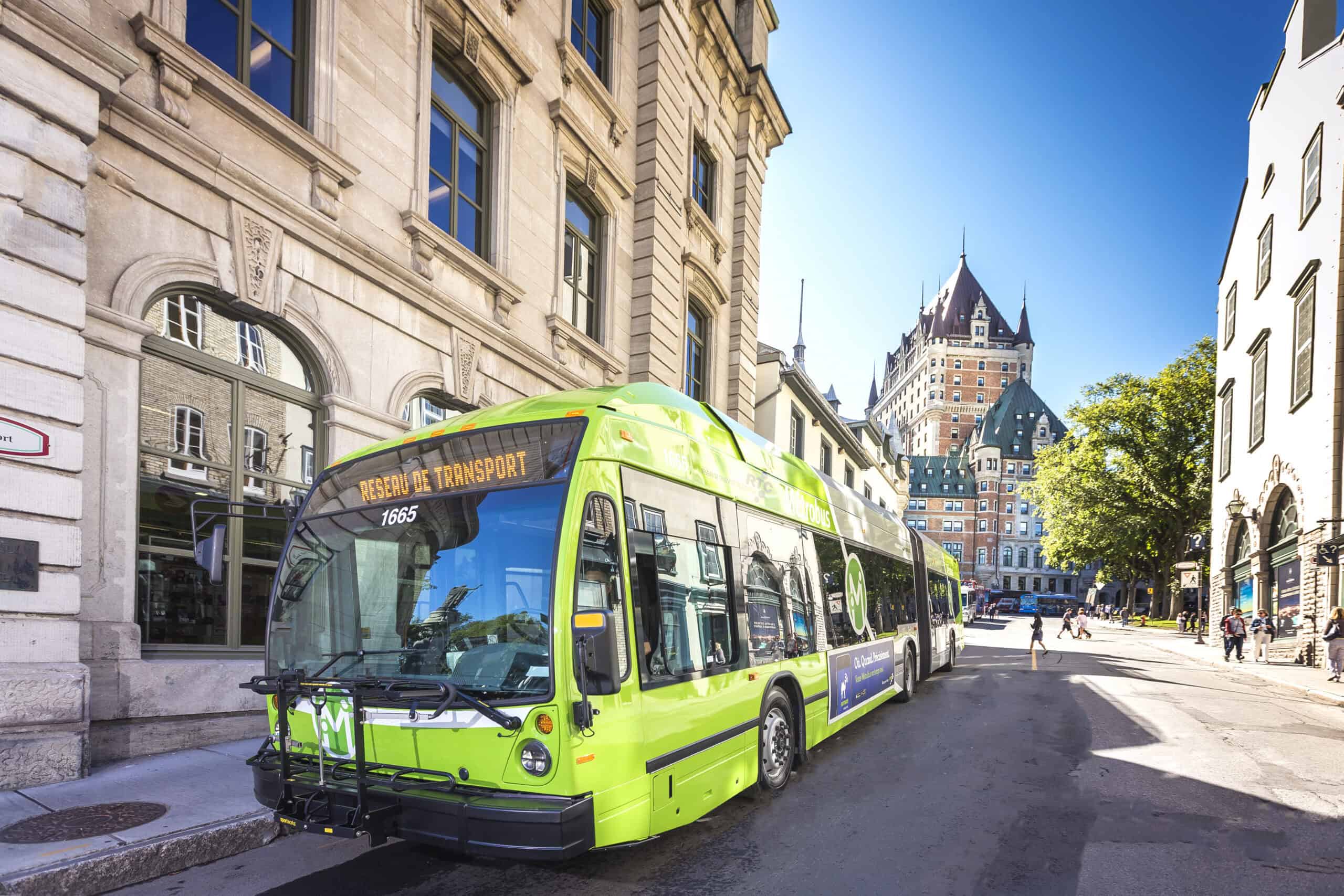 A green city bus labeled Réseau de Transport, part of Québec City Transportation Planning, is parked on a sunny street with historic buildings and Château Frontenac in the background.