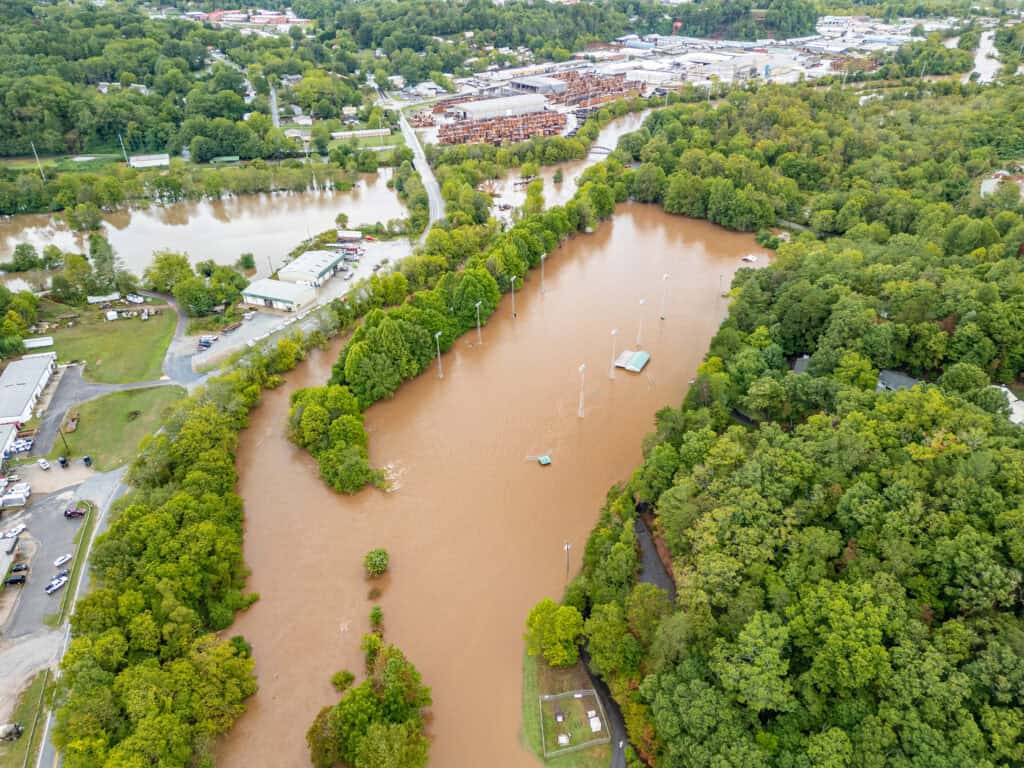 Aerial view of a flooded area in western North Carolina with muddy water, surrounded by trees and buildings.