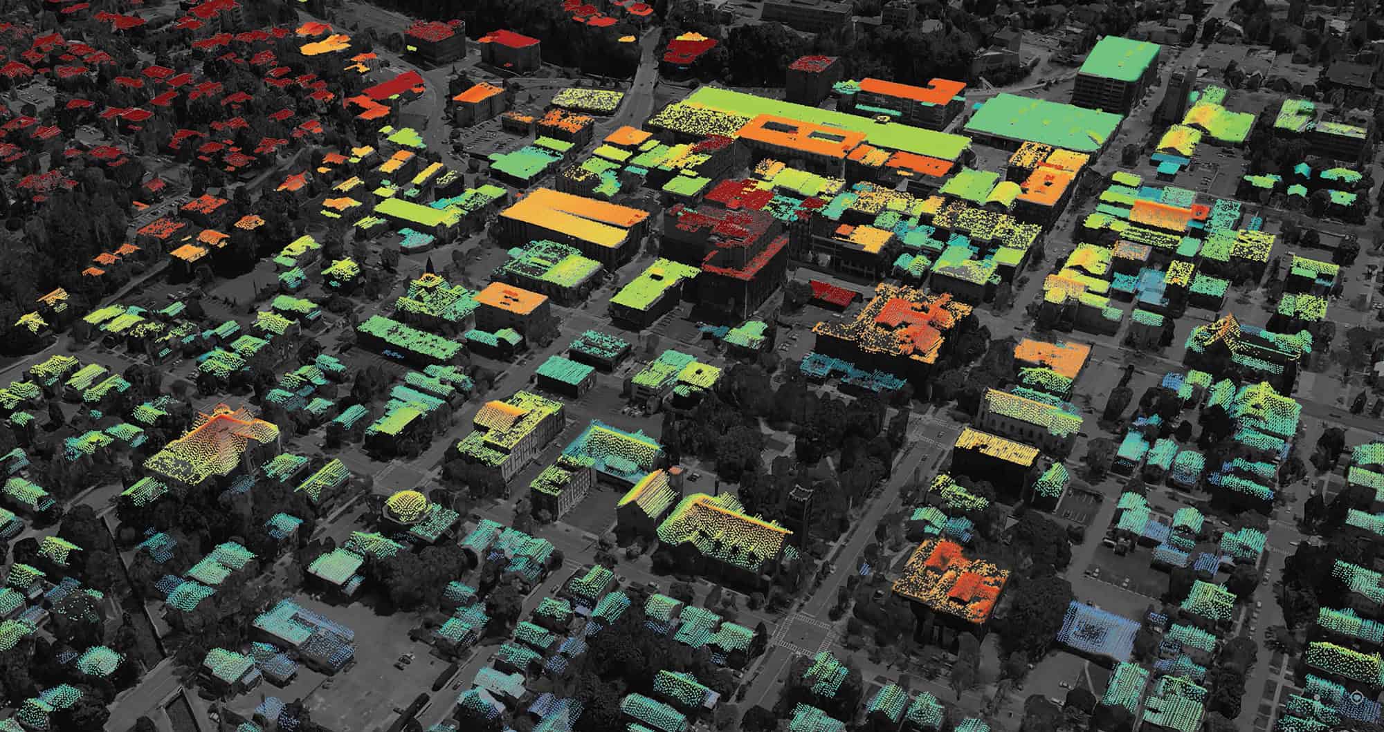 Aerial image of a city neighborhood with buildings color-coded from red to green, indicating different heights or heat levels. Streets and trees are also visible.
