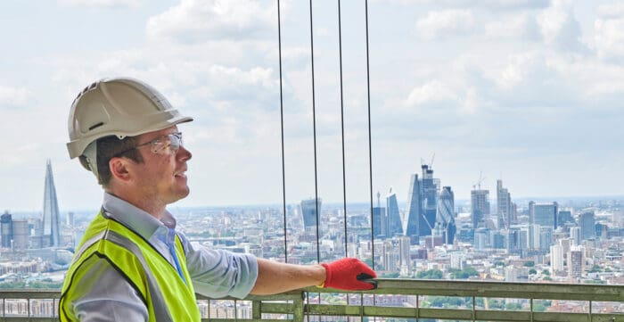 Construction worker in safety gear looks at a city skyline from a high-rise building under construction.