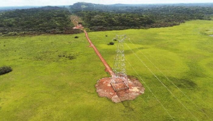 Aerial view of a transmission tower and line passing through dense forest and swampy areas.