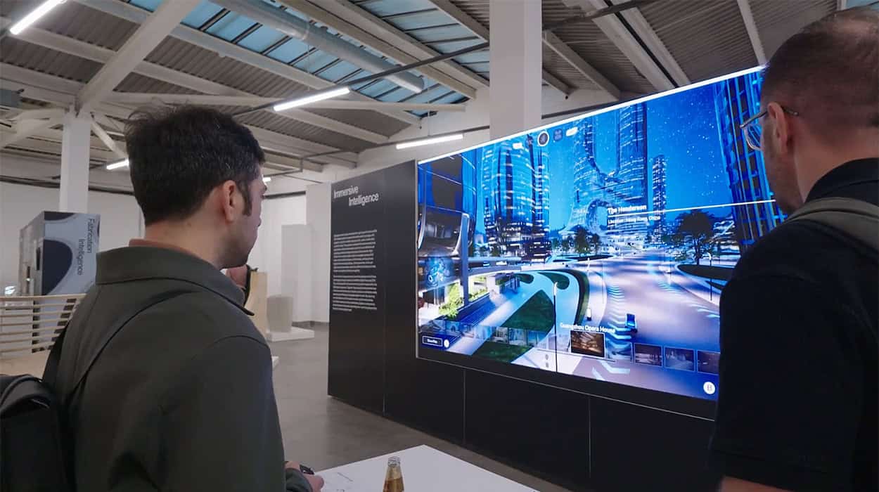 Two people view a large interactive digital display showing a futuristic cityscape inside a modern exhibition space.