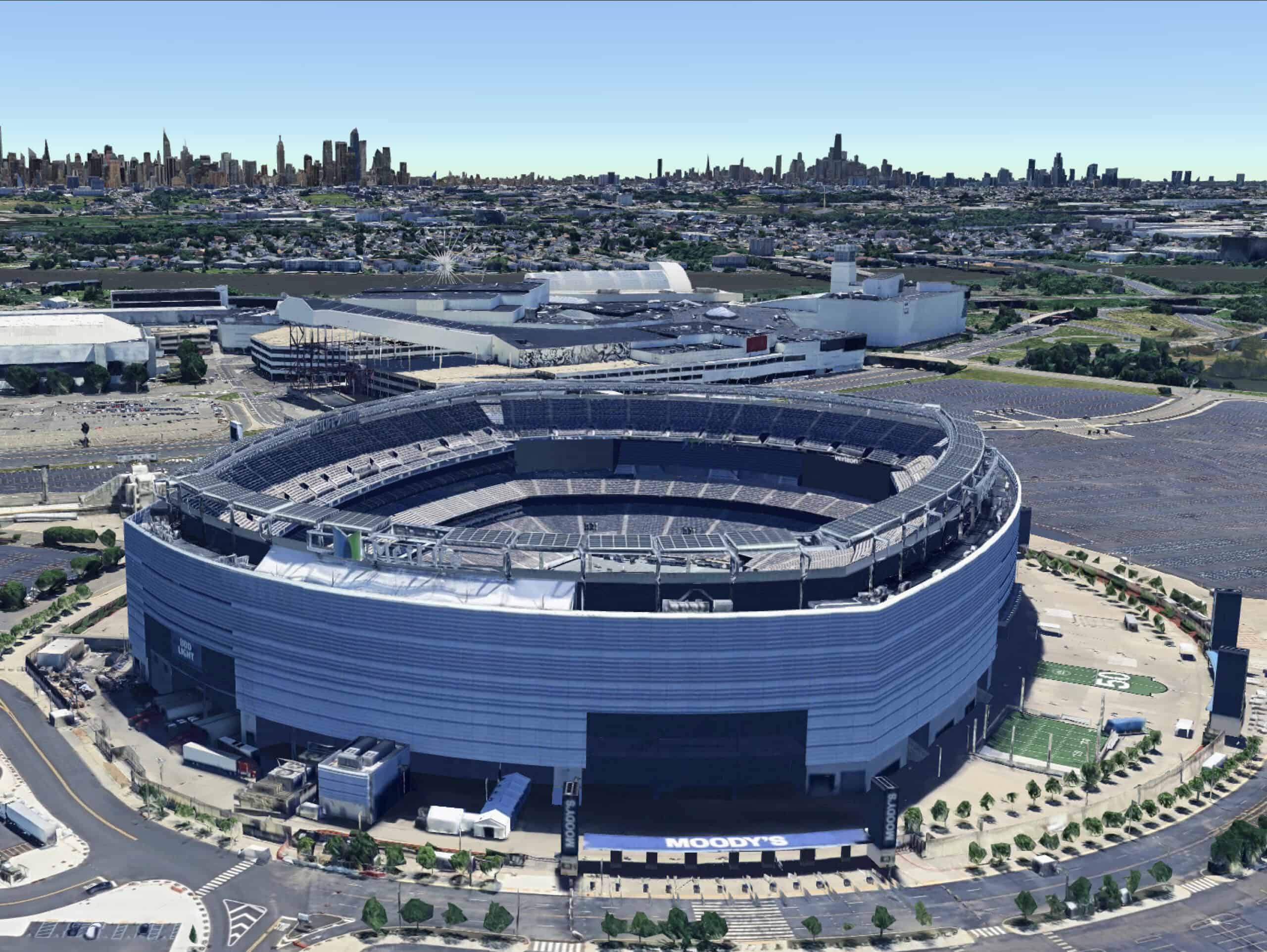 Aerial view of a large football stadium surrounded by parking lots and showcased in a 3D map with an urban skyline visible in the distant background.