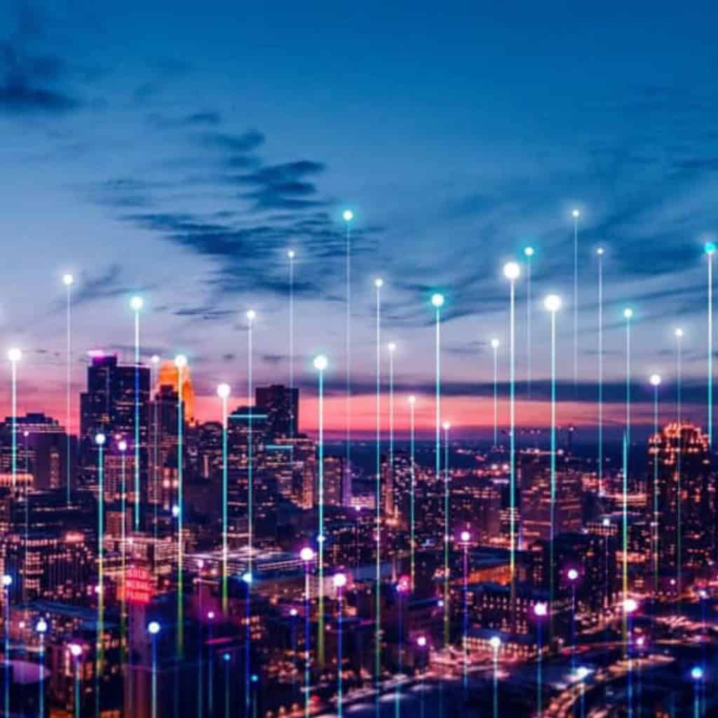 City skyline at dusk with illuminated buildings and digital lines and dots overlayed, representing the future of infrastructure, technology, and connectivity in an AI climate.