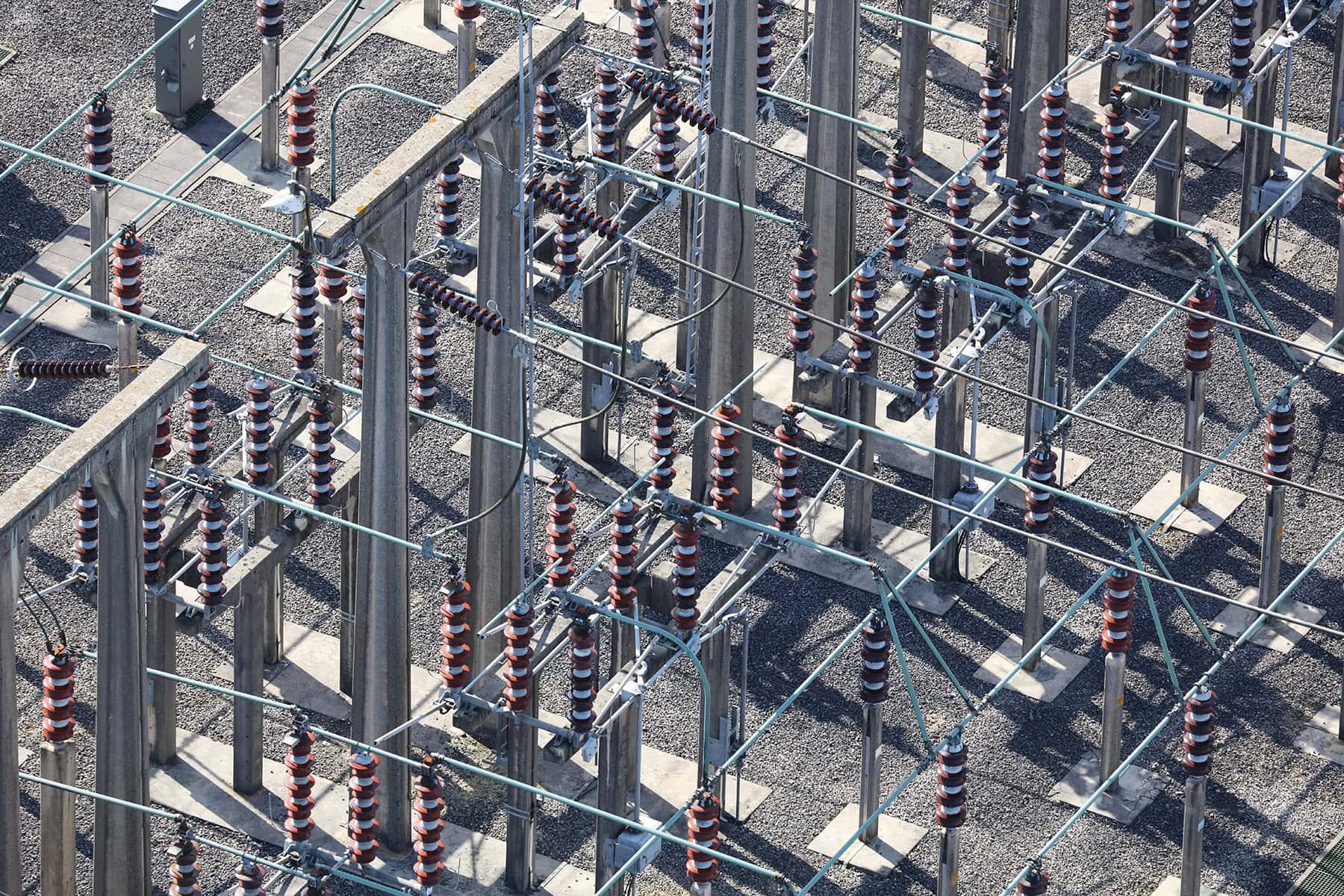 Aerial view of an electrical substation showcasing efficient substation design with numerous insulators, metal supports, wires, and a gravel ground surface.