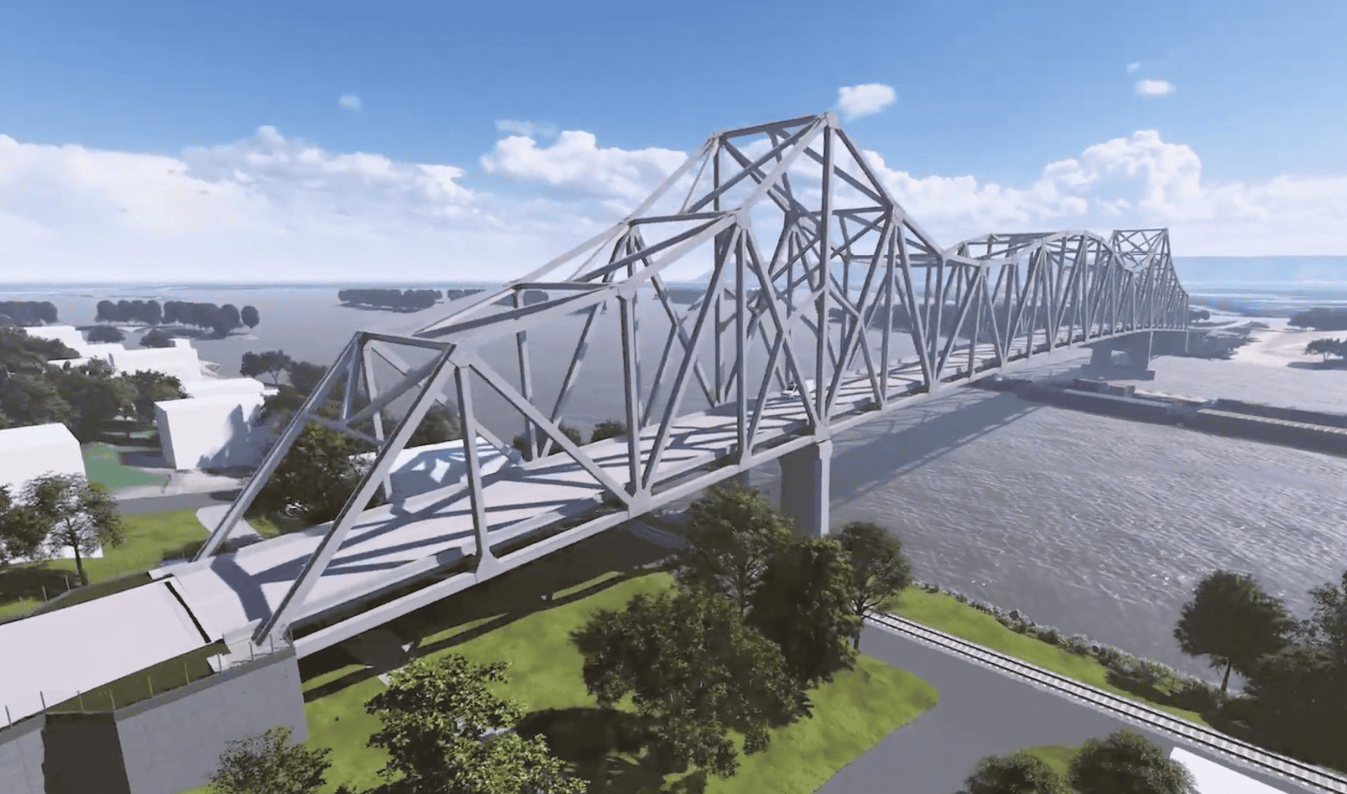 A large steel truss bridge, showcasing innovative bridge design, spans across a wide river surrounded by trees and grassy areas under a partly cloudy blue sky.
