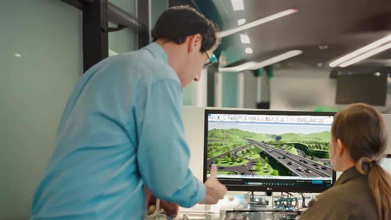 Two people review a 3D model of a highway interchange on a computer monitor in an office, sharing their vision for innovative design that aligns with Gen Z values.
