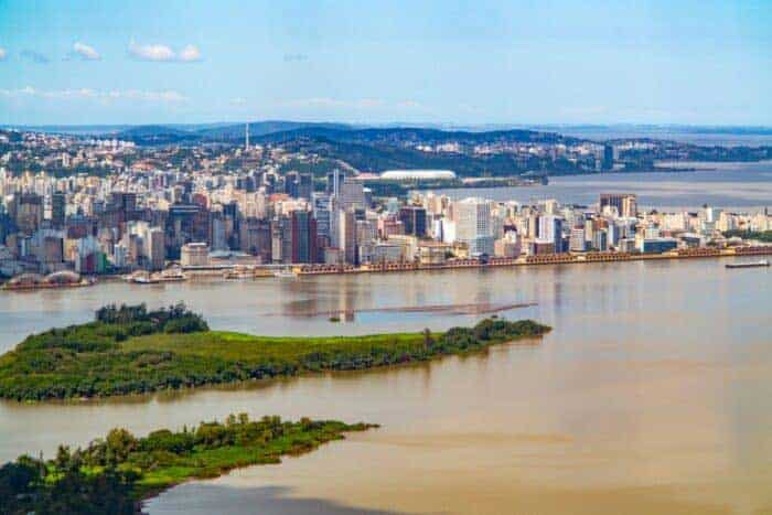 A view of a city skyline with tall buildings along the waterfront, a river featuring small green islands, and hills in the background, perfectly setting the scene for water system optimization using advanced hydraulic digital twins.