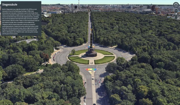 Aerial view of the Siegessäule (Victory Column) in Berlin, Germany, surrounded by a large circular road and dense green trees, with city buildings visible in the distance.