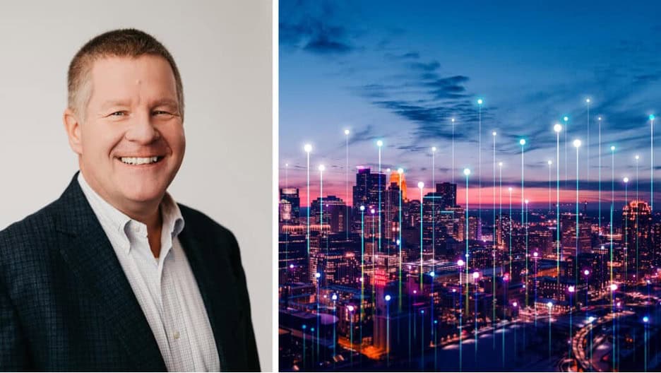 A man in a suit smiles at the camera on the left; on the right is a cityscape at sunset with digital connection lines over the buildings.