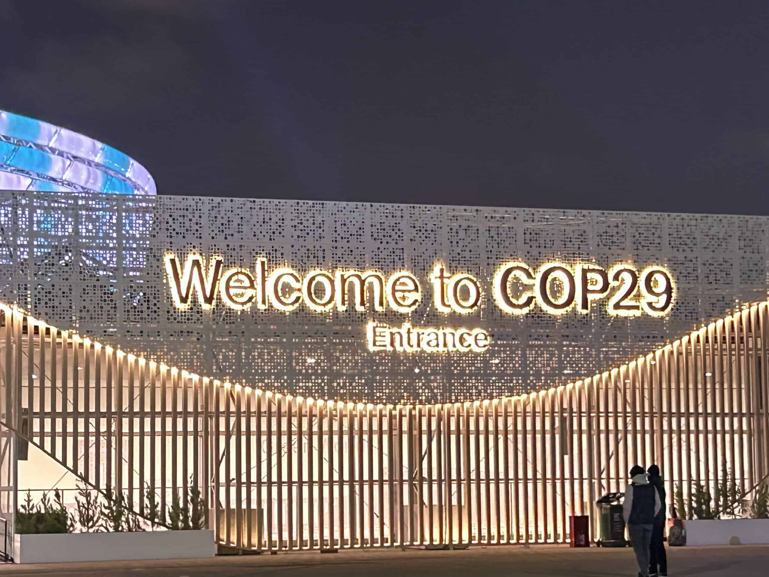 Sign with illuminated text reads Welcome to COP29 Entrance against a decorative backdrop at night.