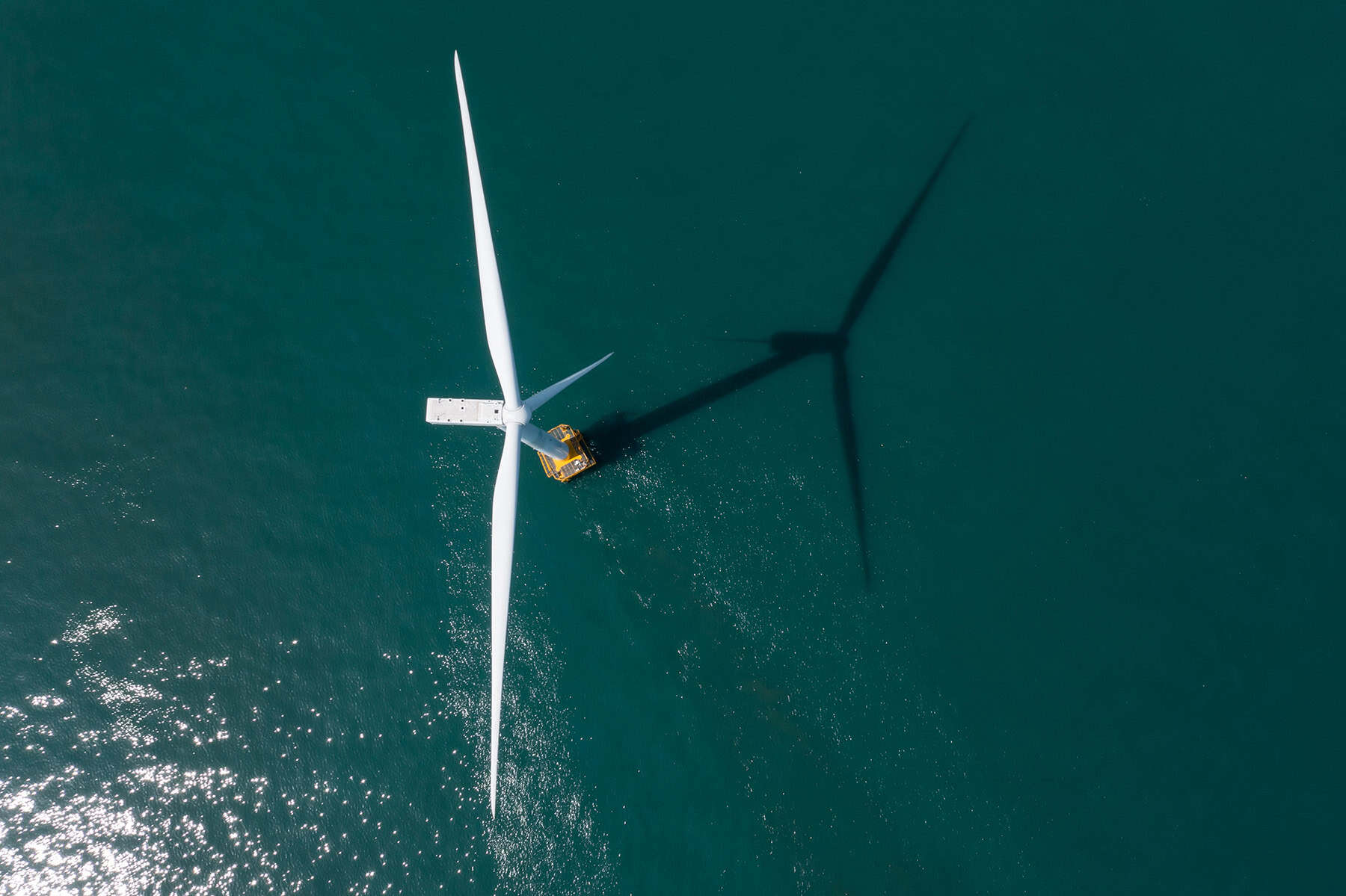 Aerial view of an offshore wind turbine with a maintenance vessel nearby, casting a long shadow across the water&mdash;ideal for integrating substation data to optimize operations and ensure efficient energy transmission.