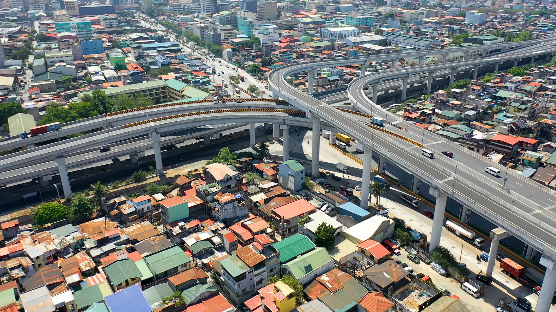 Aerial view of a multi-level highway interchange and connector road above Manila’s densely populated urban area, highlighting traffic congestion among the houses and buildings.