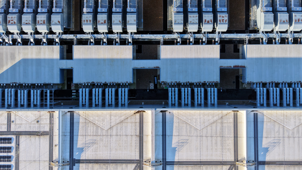 Aerial view of a modern industrial facility with rows of HVAC units and large concrete structures arranged in a geometric pattern, showcasing precise 4D planning for efficient data center delivery.
