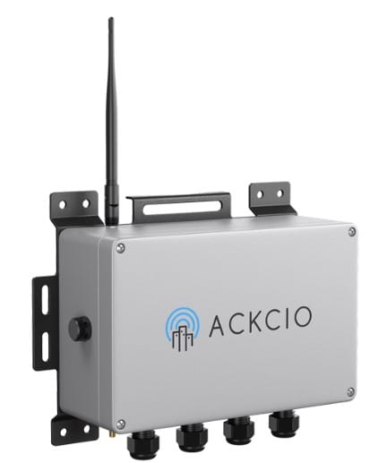 A grey rectangular device with an antenna, four cable connectors at the bottom, and the ACKCIO logo on the front, mounted on a wall bracket.