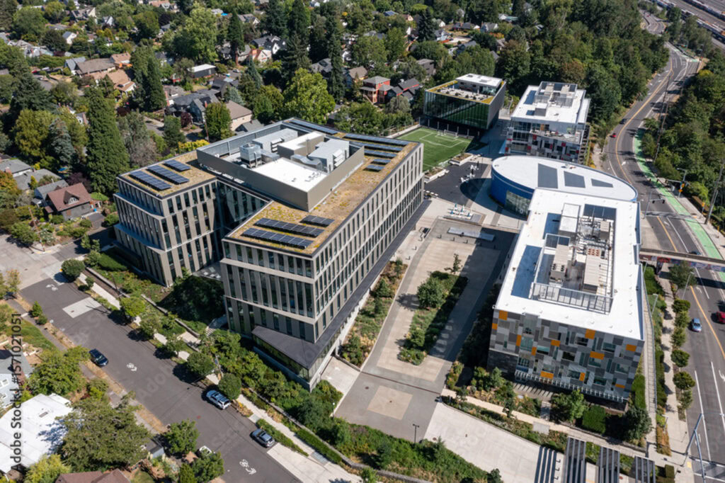 Aerial view of a modern university or office campus showcasing innovative facility buildings design, with several multi-story structures, parking areas, green spaces, and a surrounding suburban neighborhood.