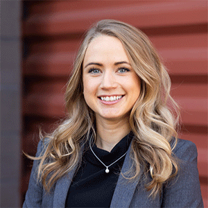 A professional portrait of a smiling woman with long blonde hair, wearing a dark blazer, against a webinar series-themed background.