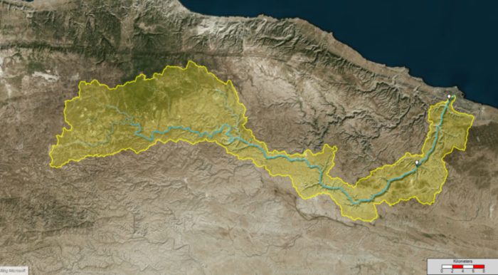 A satellite map depicting a geographical area with a blue river running through it. The area, essential for Storm and Sewer Modeling, is highlighted in yellow and bordered by different terrain. A scale in kilometers is shown at the bottom right. This map complements our OpenFlows video series for further insights.