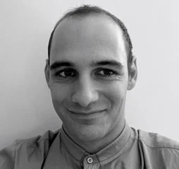 Black and white portrait of a smiling bald man wearing a collared shirt, captured during a webinar on cloud technology.