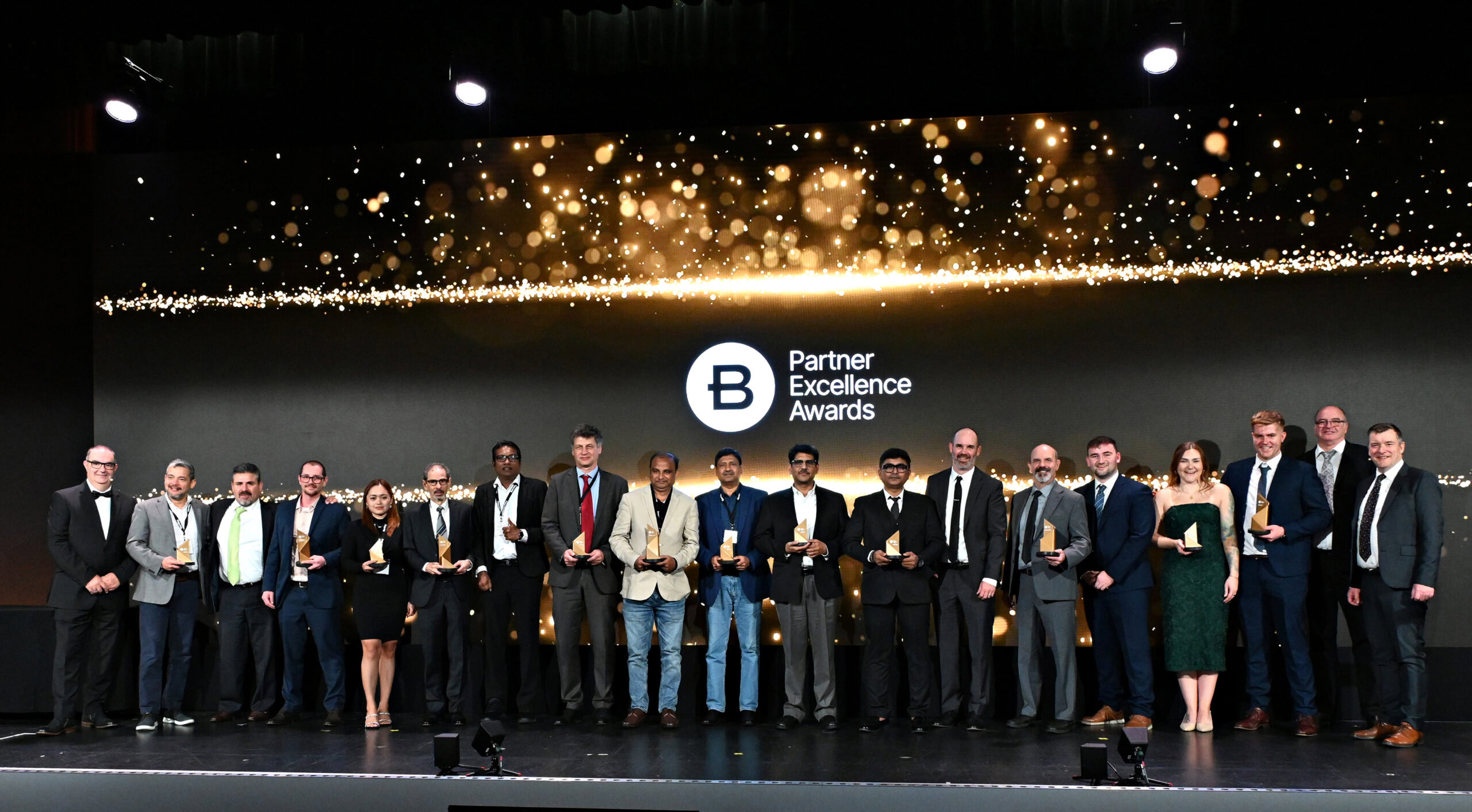A group of Award Winners stand on stage holding awards in front of a screen displaying "Partner Excellence Awards".