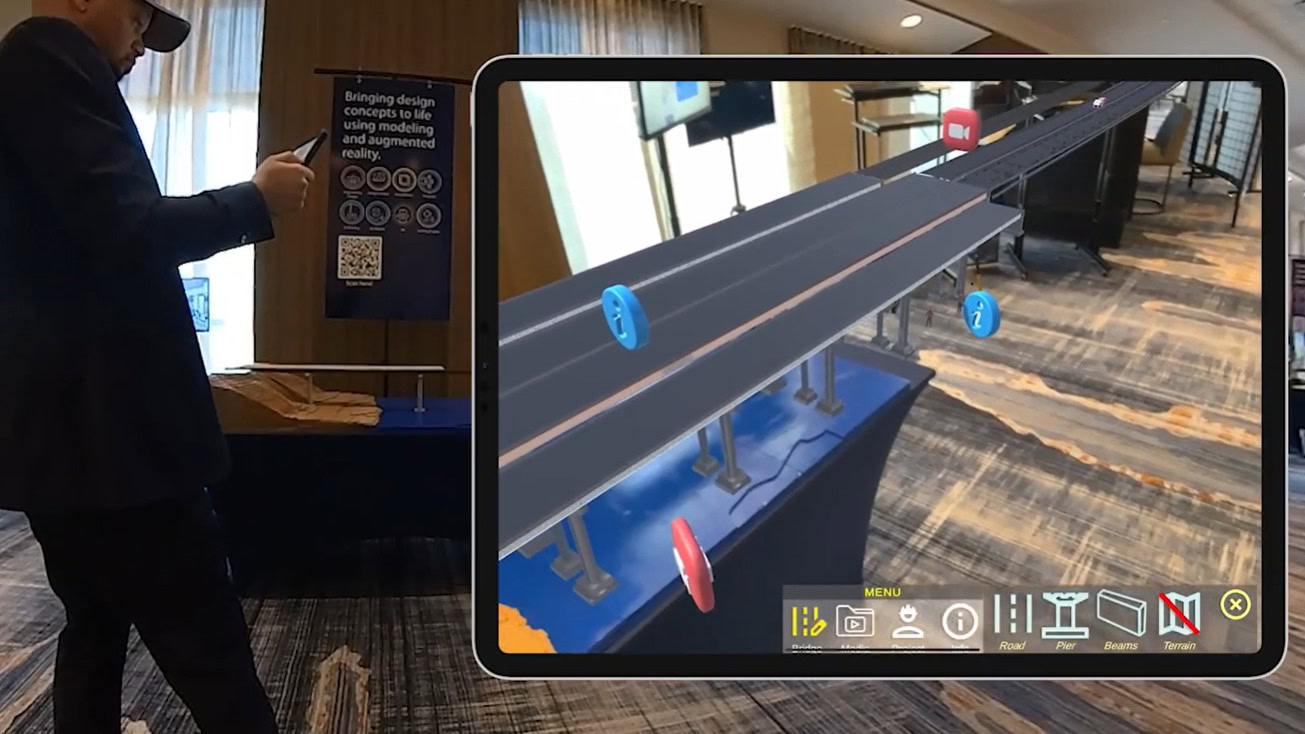 A person holds a tablet displaying an augmented reality conveyor belt with colored tokens, in a conference or exhibition setting focused on bridge and tunnel engineering.