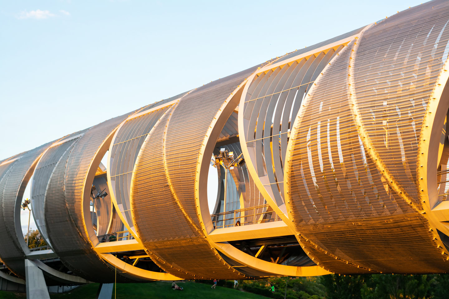 A close-up of a modern pedestrian bridge with a metallic, spiraled design illuminated by sunlight, showcasing the innovative architecture that bridges the gap between traditional structures and futuristic operations.