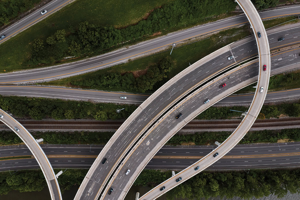 Aerial view of a multi-level highway interchange with several cars traveling on curved and straight roads, designed using MicroStation software, surrounded by greenery.