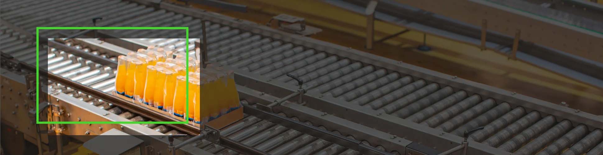 Bottles of orange liquid are being transported on a conveyor belt inside a manufacturing plant. The highlighted section shows a group of six bottles.