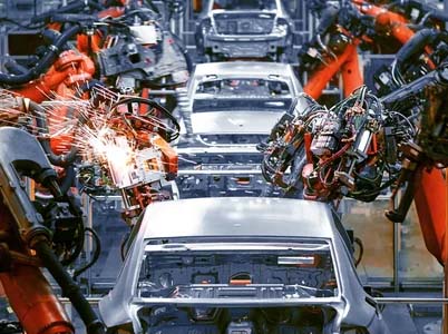 Industrial robots work on automobile assembly in a manufacturing plant, with sparks flying from a welding process on car bodies.