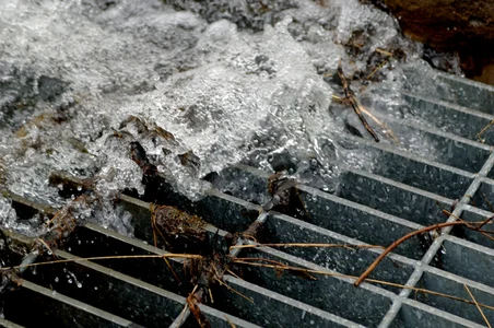 Water flows over a metal grate, carrying debris and sticks, illustrating concepts from the OpenFlows Storm and Sewer Modeling short video series.