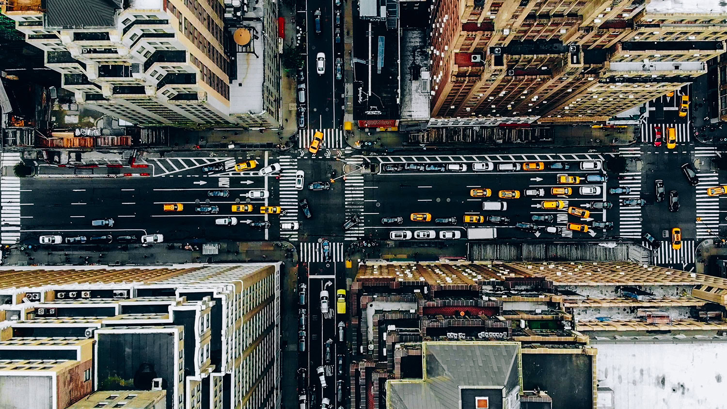 Aerial view of a busy city intersection with yellow taxis, cars, and pedestrians surrounded by tall buildings, revealing OpenPaths Patterns in urban movement.