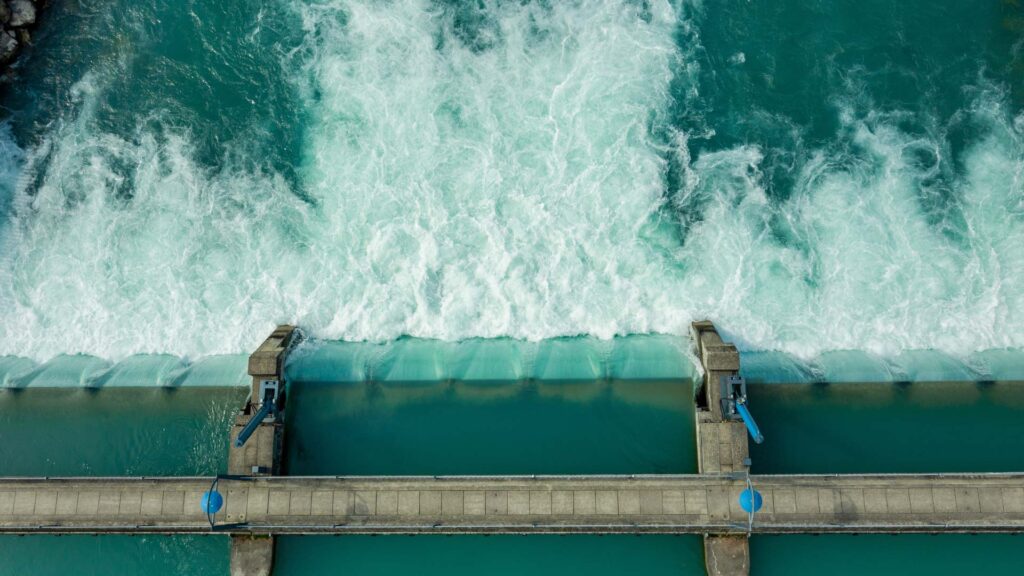 Aerial view of water flowing over a dam, highlighting the cascading water and the concrete structure beneath. Using OpenFlows technology enhances risk management by providing vital insights to reduce risk.