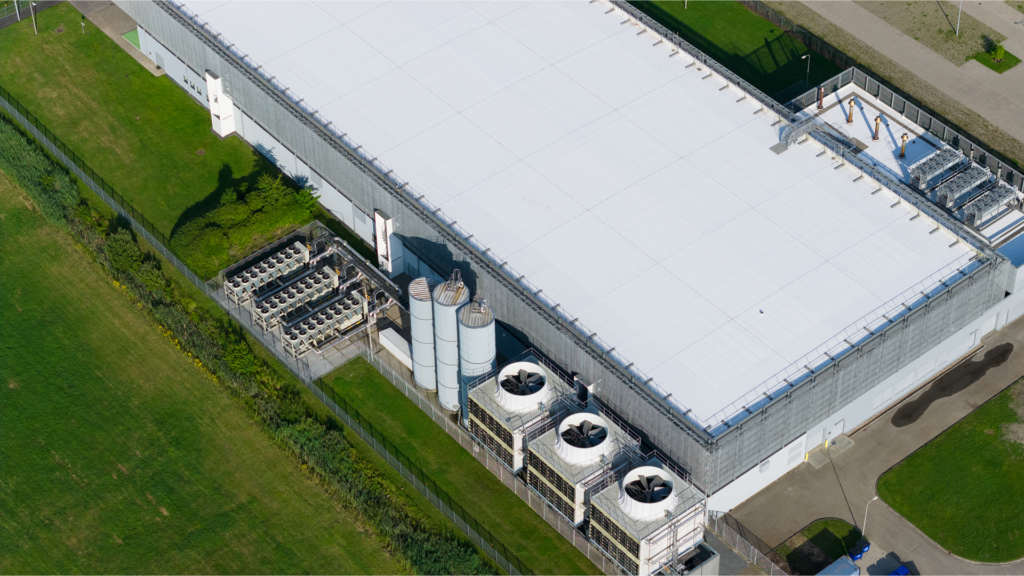 Aerial view of an industrial building with a white roof, large ventilation fans, cylindrical tanks, and grassy areas—ideal features often seen in modern data centers.